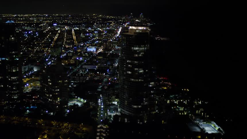 A mesmerizing night-time aerial approach and orbit of Portofino Tower and surrounding skyscrapers in South Beach Florida