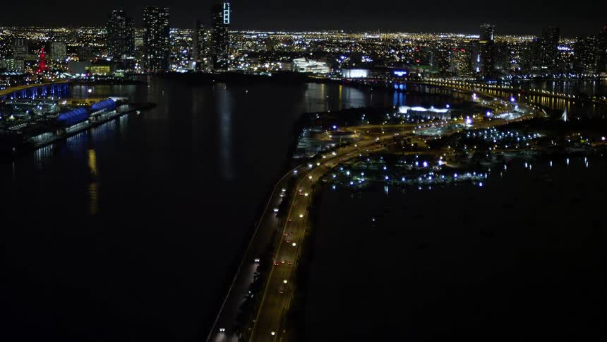The aerial footage captures a stunning nighttime view of Downtown Miamis skyscrapers as the camera tilts up from the MacArthur Causeway