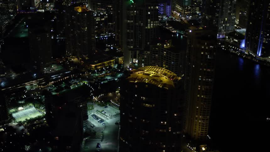 The camera orbits around a skyscrapers rooftop on Brickell Key at night in Downtown Miami Florida capturing the metropolis and clear skies of the city below