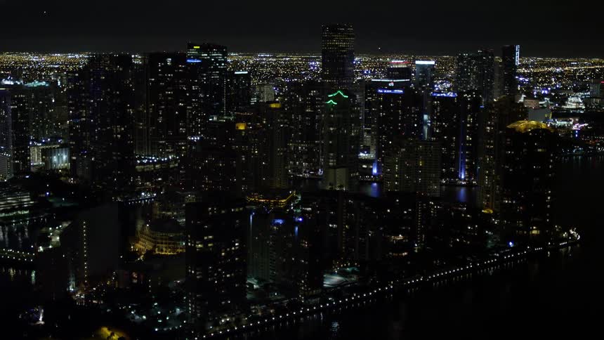 An aerial view of illuminated skyscrapers and buildings in Downtown Miami Florida at night including Brickell Key high-rises near the river