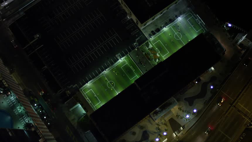 A stunning birds eye view of soccer games being played at night on multiple fields with city lights shining down on them in downtown Miami Florida