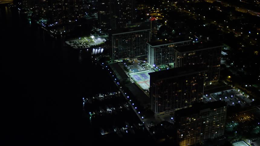 An aerial view of illuminated waterfront apartment buildings at night in Downtown Miami Florida approached by the camera