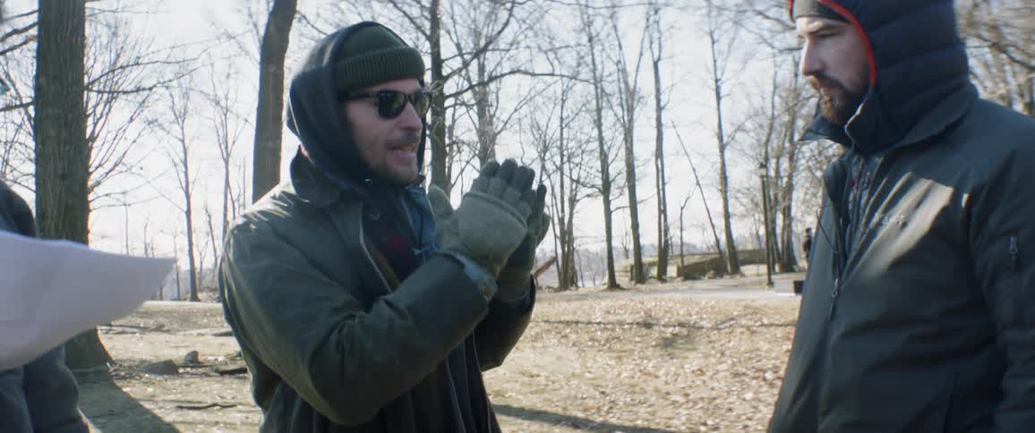 Man talks and gestures to another man outside on a sunny cold day