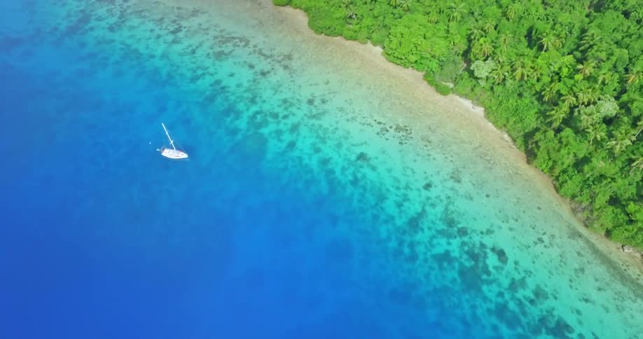 A sailboat rests in brilliant blue waters off a coastline