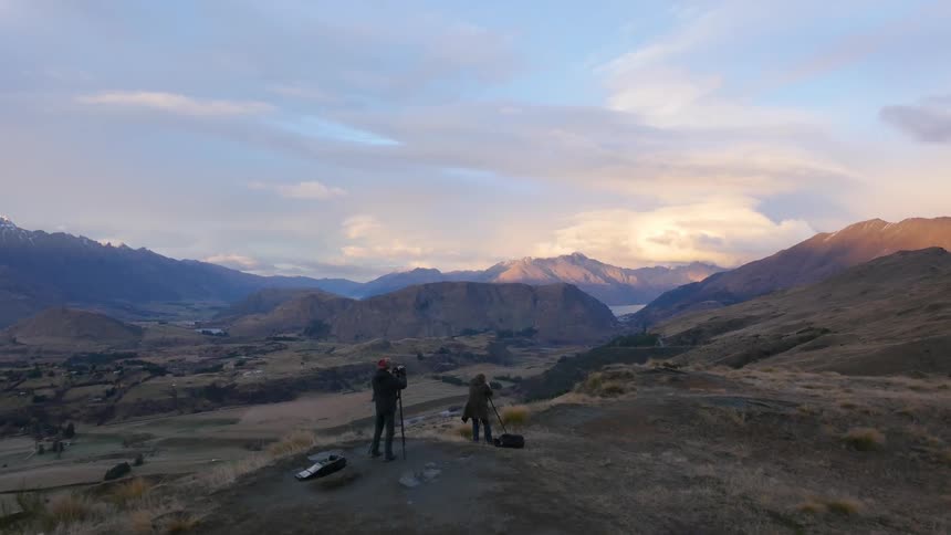 Two people set up tripods and cameras on a hilltop