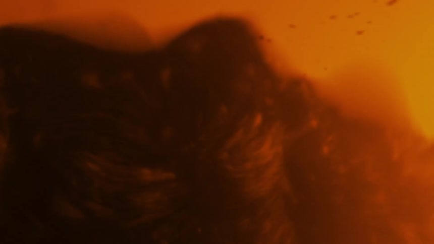 A thick red substance splashes and splatters as droplets fly in the orange liquid