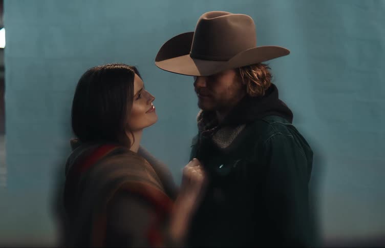 Man with cowboy hat beard and jacket looks into womans eyes lovingly