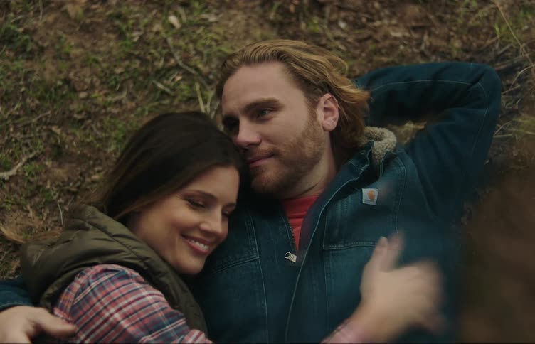 A man is lying on the ground outside with his arm around his girlfriend as she lies next to him