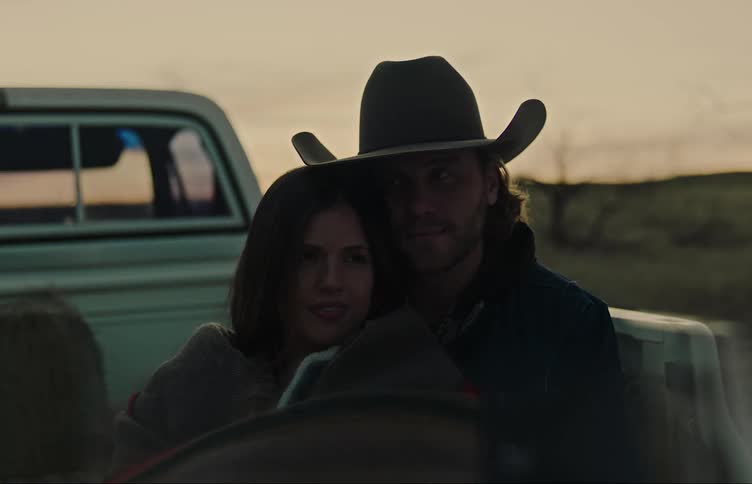 A man kisses his wife on the cheek while sitting in the bed of a pickup truck