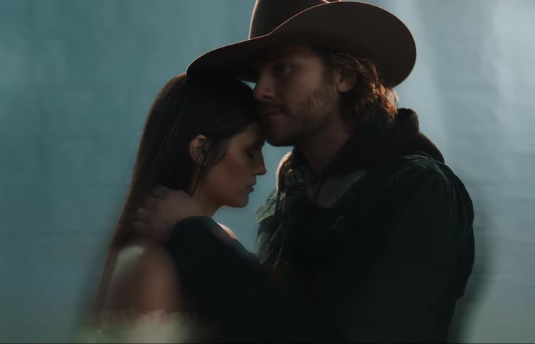 A man and woman are facing each other as he has his chin resting on her forehead and his hand on her shoulder