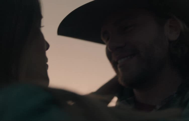 Woman caresses face of man and adjusts his clothes while they stand in field near pickup truck