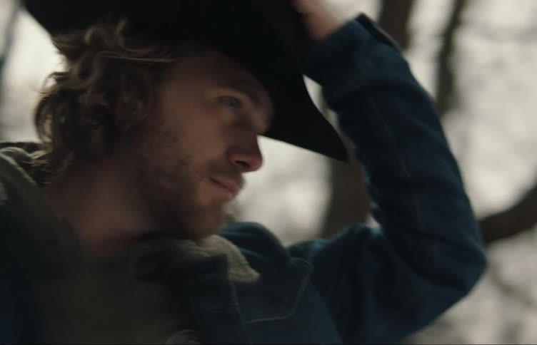 A cowboy takes off his hat runs his hand through his hair puts the hat back on and looks back over his shoulder