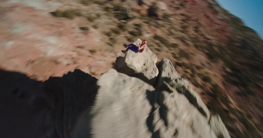Orbiting aerial view of a woman sitting atop a rock formation in the badlands