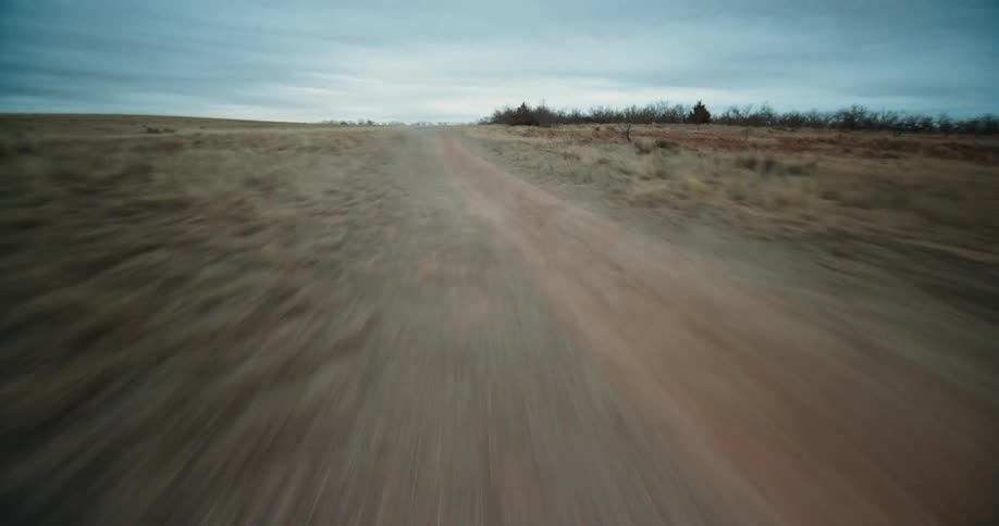 Red jeep drives quickly along dirt road through countryside under an overcast sky