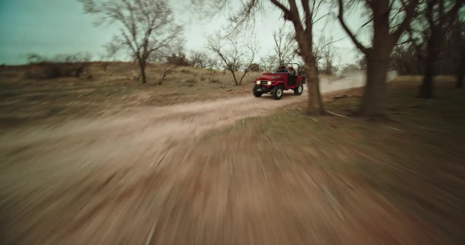 A time lapse of people driving a jeep down a desert dirt road with trees on either side