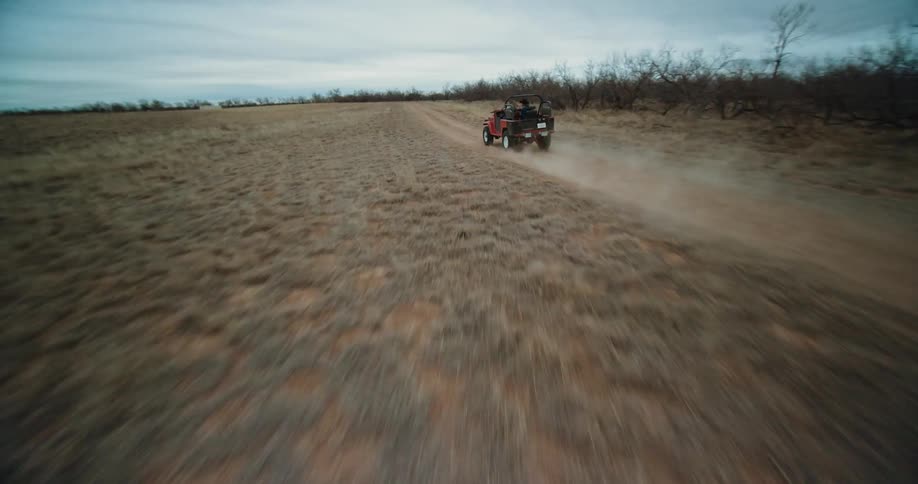 Two men ride a jeep down a dirt road