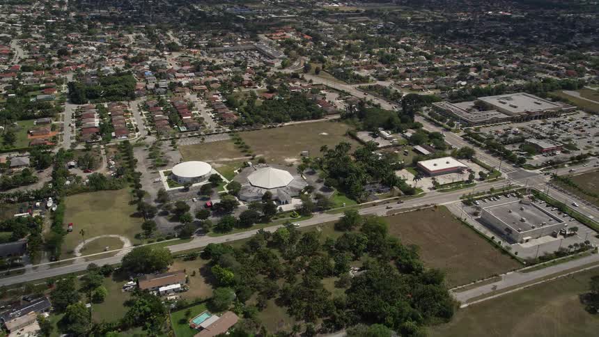 Approaching the Upper Room Assembly of God in South Miami Heights Florida during a partly cloudy day from an aerial viewpoint