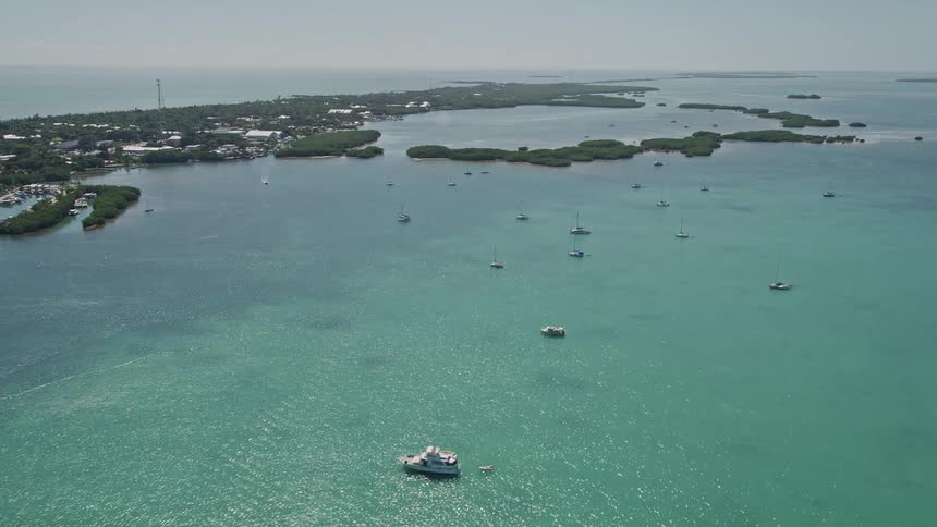 This aerial footage captures fishing boats and sailboats in Islamorada Florida as the drone flies over them towards the shoreline