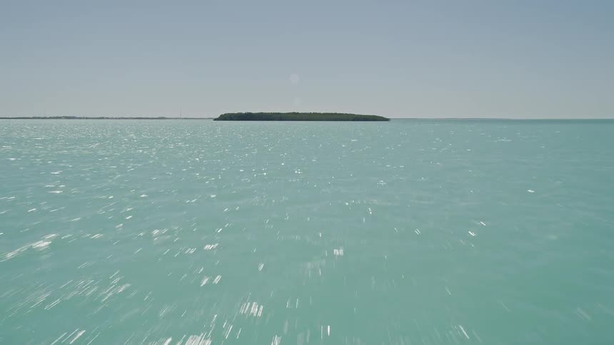 Flying over the water of Tavernier Florida tilting up to reveal mangroves near the shore and a tree-covered island in the middle of the sea during daytime in Floridas summer