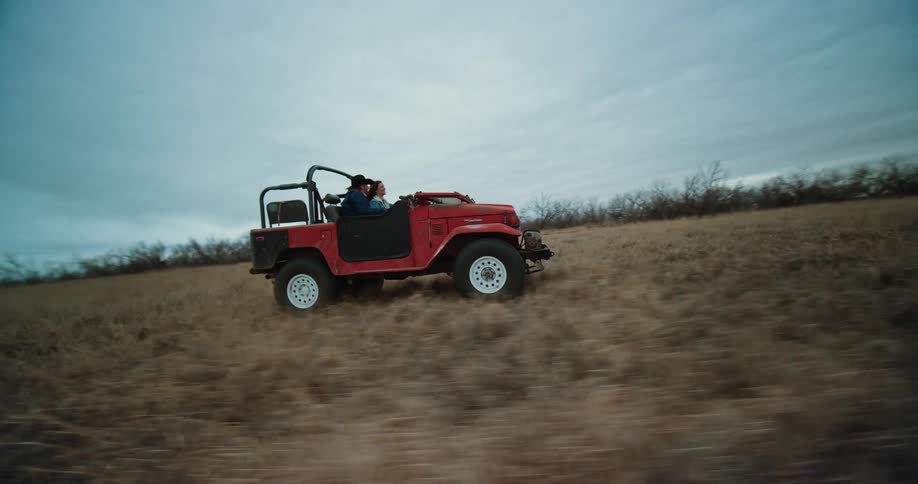A man and woman ride a jeep through an open field