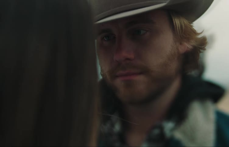 Close up of the face of a man wearing a cowboy hat hugging a woman in the countryside