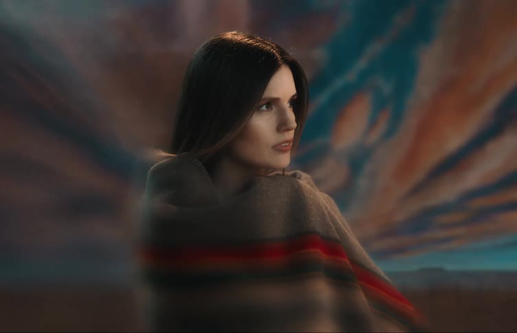 A woman stands with a patterned blanket around her shoulders