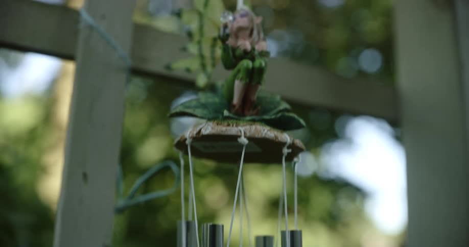 Fairy figure topped wind chimes sway near reflective window