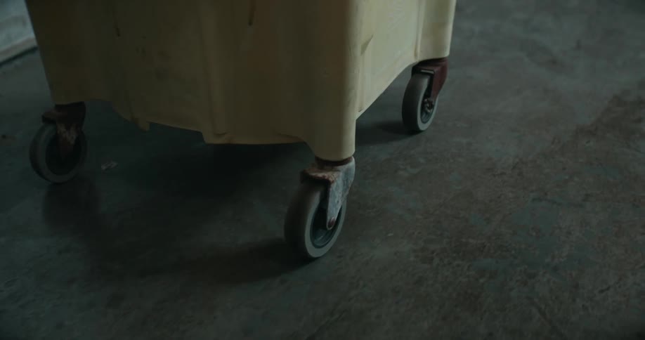 Person walks along concrete floor pushing a wheeled mop bucket