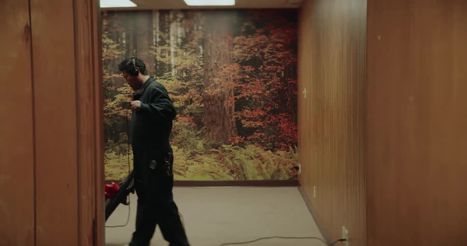 Man wearing headphones vacuums in a room in front of a mural of trees