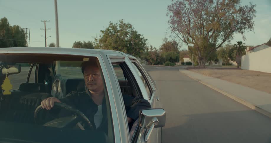 Man drives car down a street in the suburbs as seen through a vignette lens
