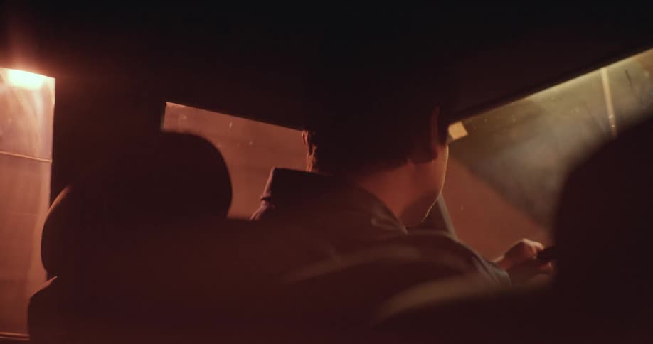 Light shines on an automobile windshield as a man drives at night