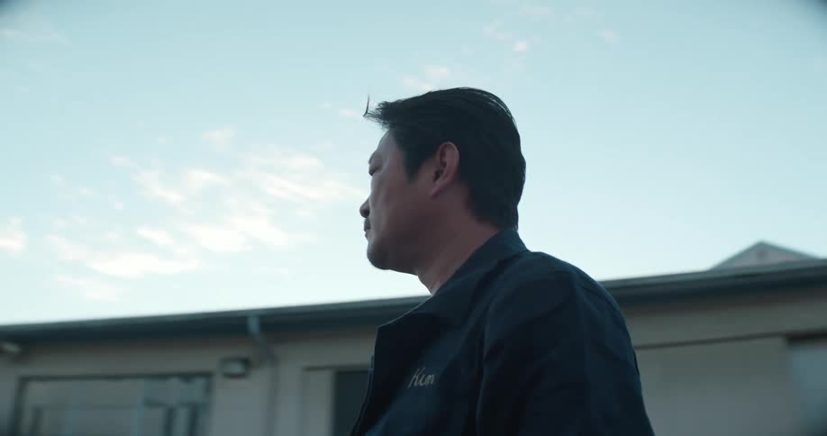A man is outside walking near buildings when he stops to stare at something then turns and walks away
