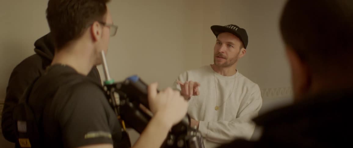 People are talking in a room and one is holding a camera