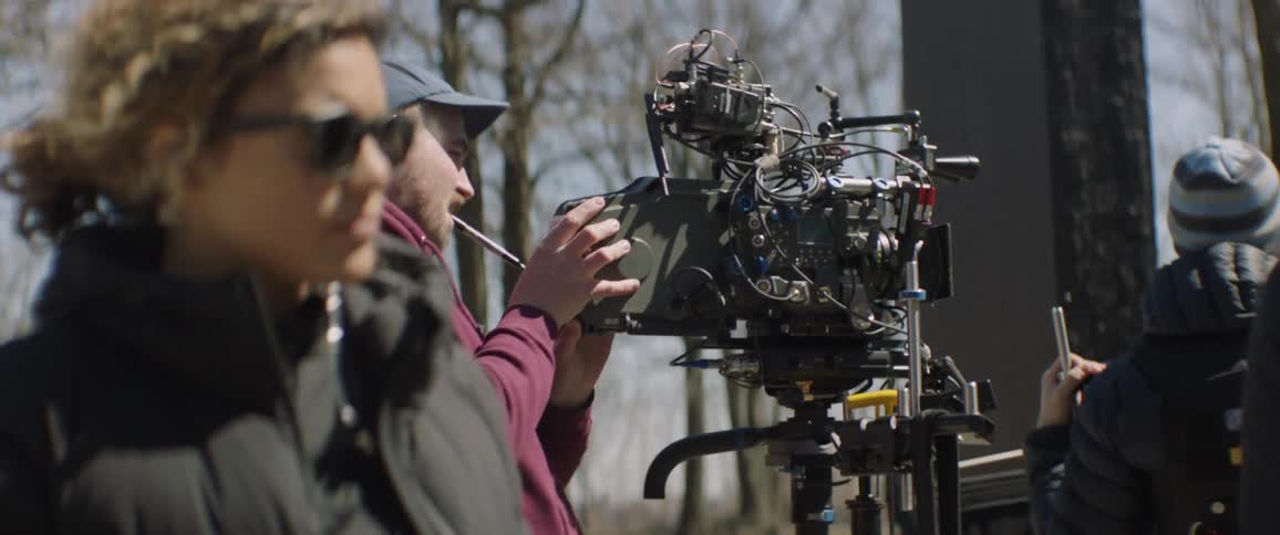 A woman stands next to a cameraman on an outdoor set
