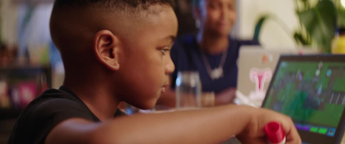 A boy uses a marker to color in a coloring book before turning to play a game on a laptop