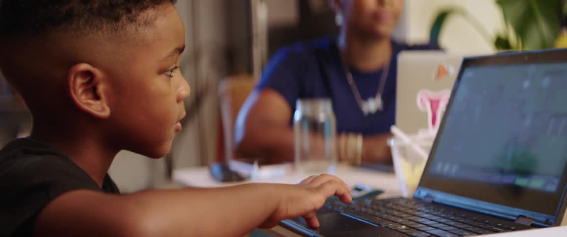A mother and son use laptops at the kitchen table