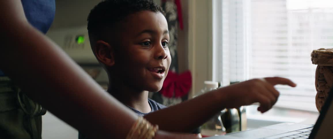 A woman points out something on a laptop screen to a boy who mimics her pointing