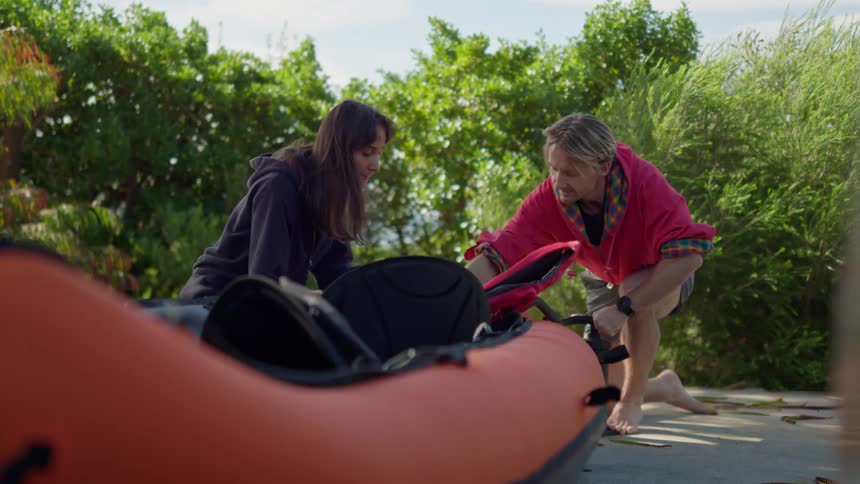 A man pumps air into a rubber boat while a woman watches and he gives her a high five when he finishes