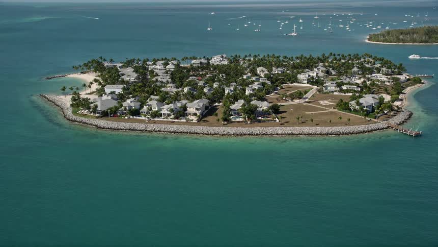 Aerial footage of luxurious mansions on Sunset Key Florida surrounded by crystal blue waters and sailboats passing by