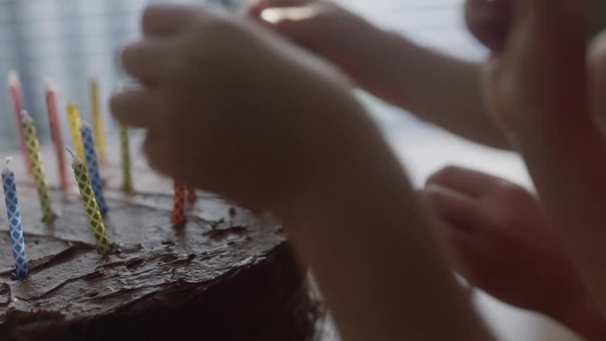 Two young girls place birthday candles on a chocolate frosted cake
