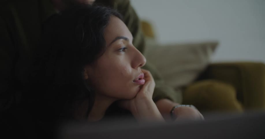 A woman is sitting on the floor as a man is sitting on the couch behind her looking over her head