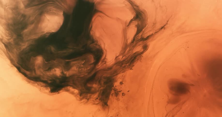 Black liquid falls into an orange substance and spreads across the surface as it mixes