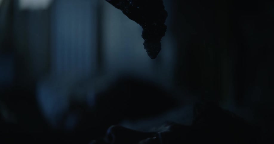 Dim light shines on the face of a man lying awake in bed at night as an ominous dark organic liquid moves down over him