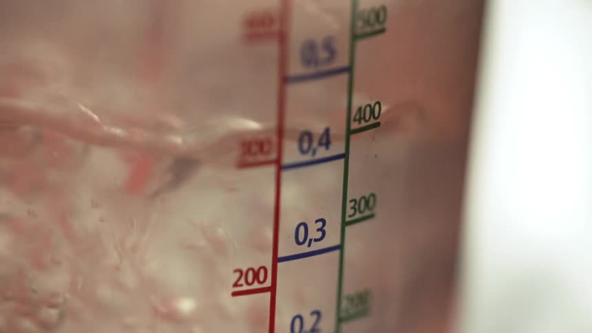 Water is being poured into a glass measuring cup shown very close up