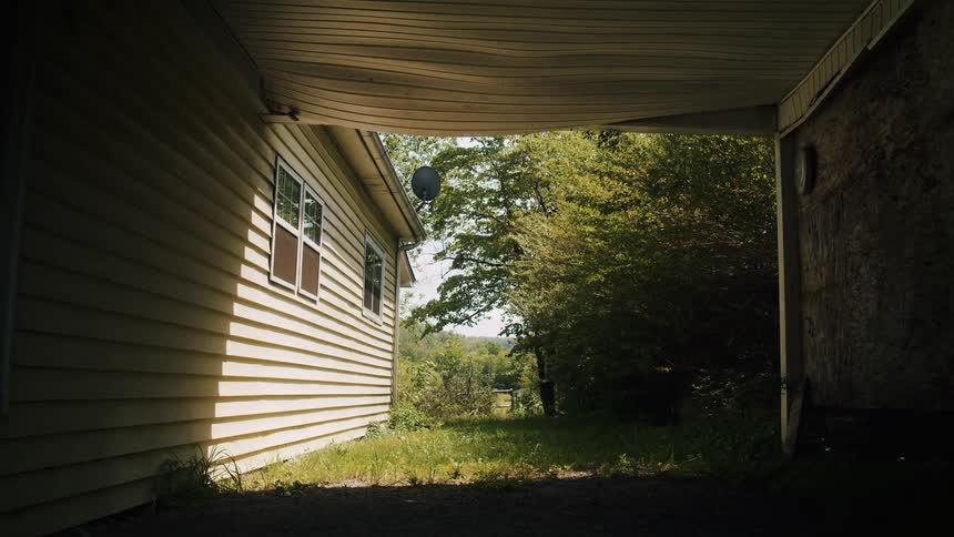 The wind causes the trees to sway that are growing along side a house