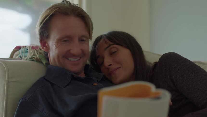 While lying on a couch a couple nestles together while reading a magazine