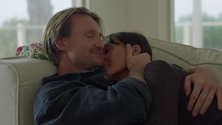 A couple embraces kisses and hold hands while lying on a living room couch