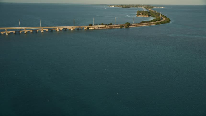 Flying over Craig Key on the Overseas Highway revealing the coastal road and large bridge spanning across Atlantic Ocean during sunset in South Florida