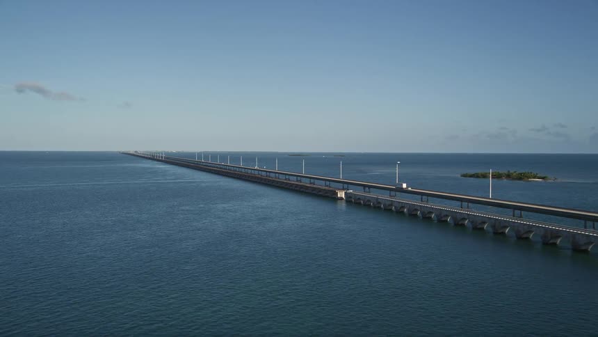 Aerial footage of a truck driving on the iconic Seven Mile Bridge in Florida as traffic moves both ways along the long causeway beside white utility poles carrying power lines