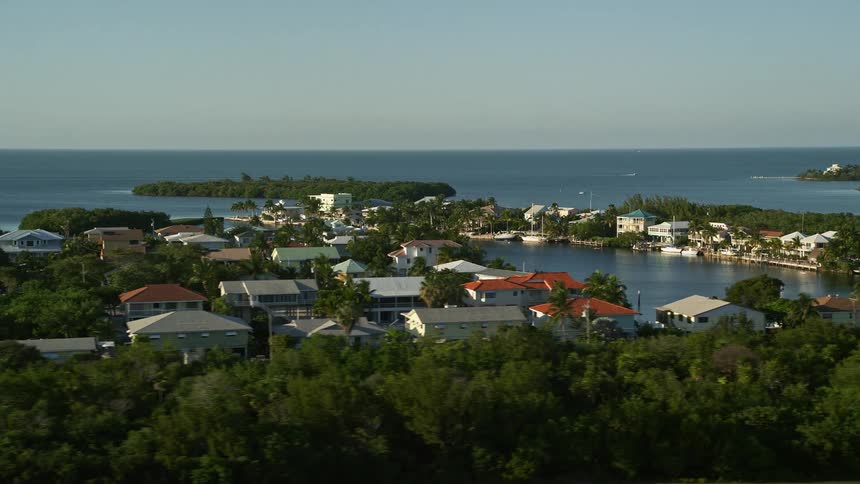 Aerial footage of residential neighborhoods and oceanfront properties with boats docked outside of houses and sailing on the water captured at dusk in Marathon Florida along the Atlantic Ocean
